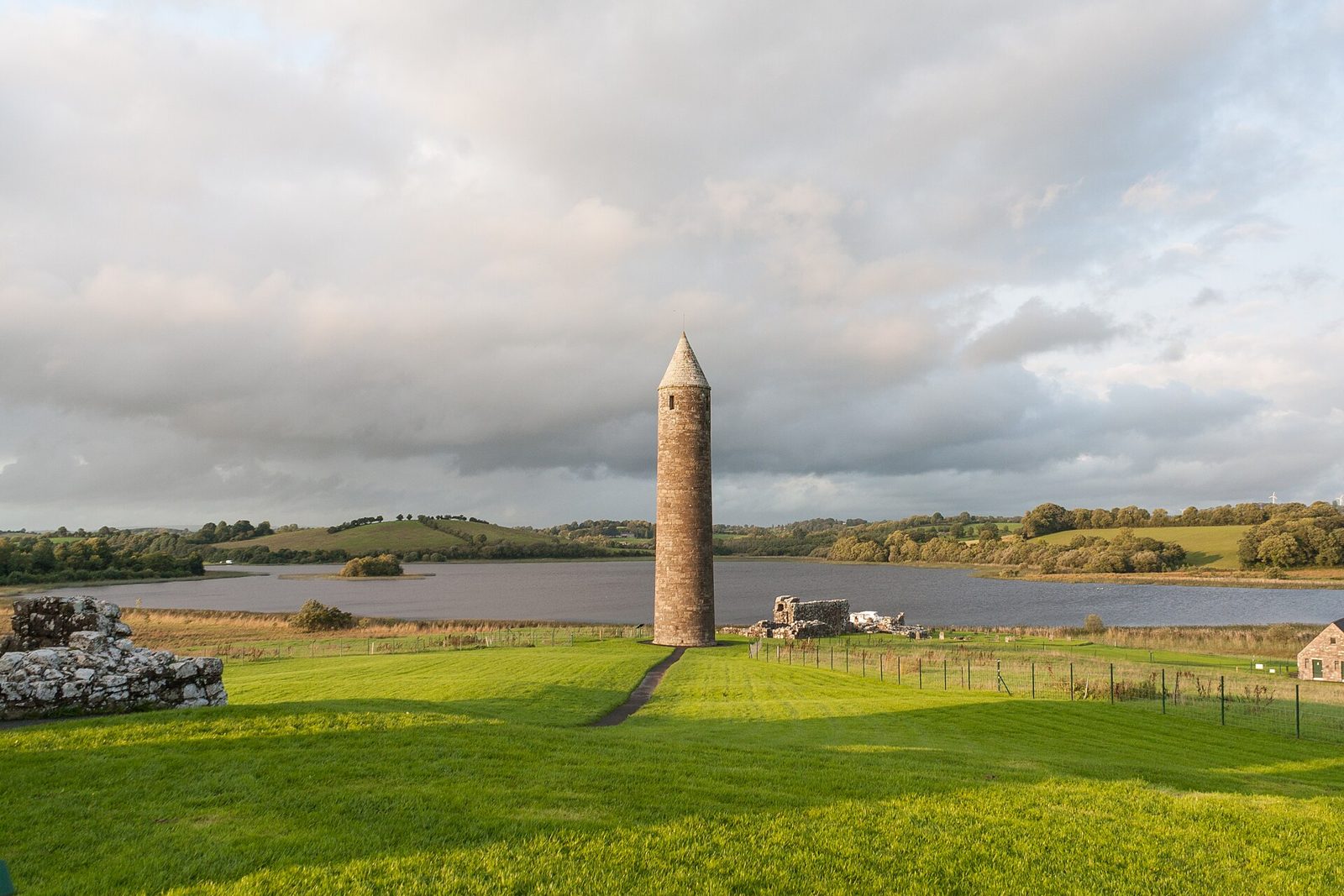 The round tower on Devenish Island standing above bright green grass with Lough Erne behind