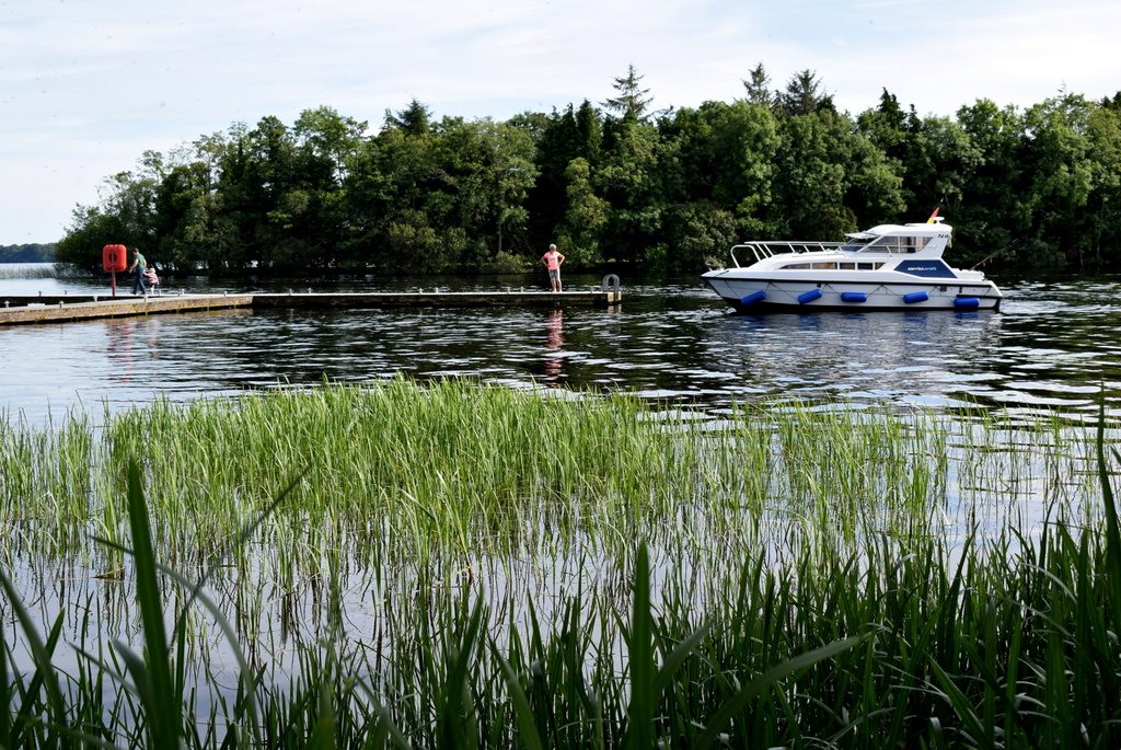 A hire cruiser on bright open water beside a green wooded island on Lough Erne