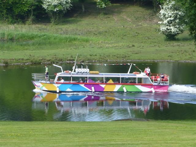 A tour boat under way on Lough Erne beside a green wooded shore